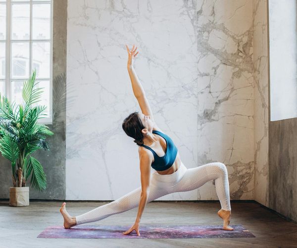 Woman performing a gentle stretching exercise in a calm, sunlit room.